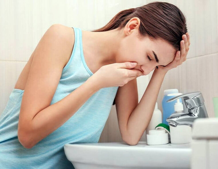 Uma mulher com enjoo de gravidez, vomitando na pia do banheiro.