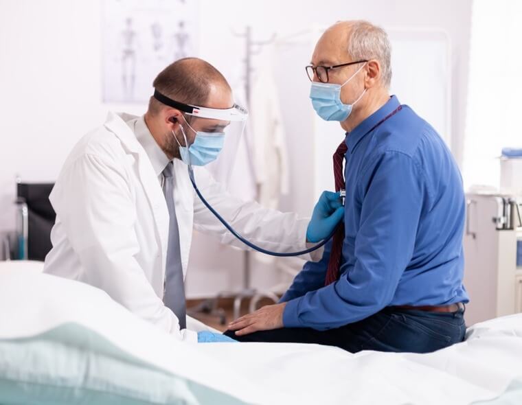 Um médico examinando um paciente que está sentado em uma maca no hospital.