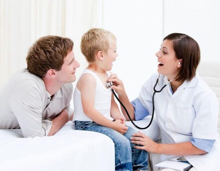 Médica examinado um menino que está acompanhado de seu pai, durante uma consulta médica.